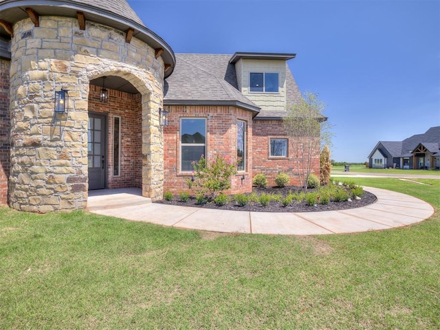 view of front of property with brick siding, a shingled roof, stone siding, and a front yard