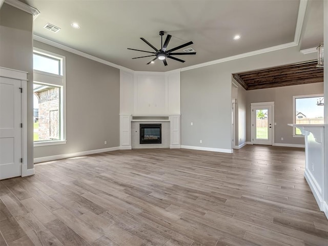 unfurnished living room featuring a wealth of natural light, ornamental molding, a glass covered fireplace, and a ceiling fan