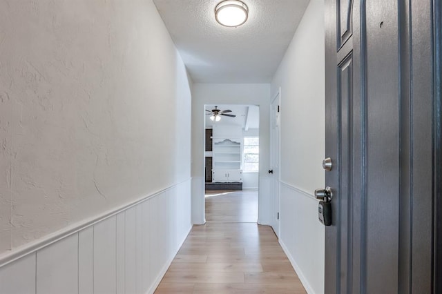 corridor with light wood-type flooring and a textured ceiling