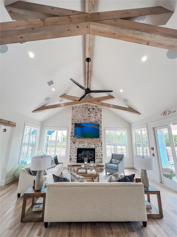 living room featuring wood finished floors, visible vents, lofted ceiling with beams, ceiling fan, and a large fireplace