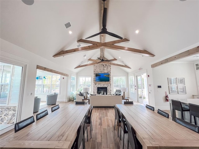 dining area with visible vents, high vaulted ceiling, beam ceiling, hardwood / wood-style flooring, and a large fireplace