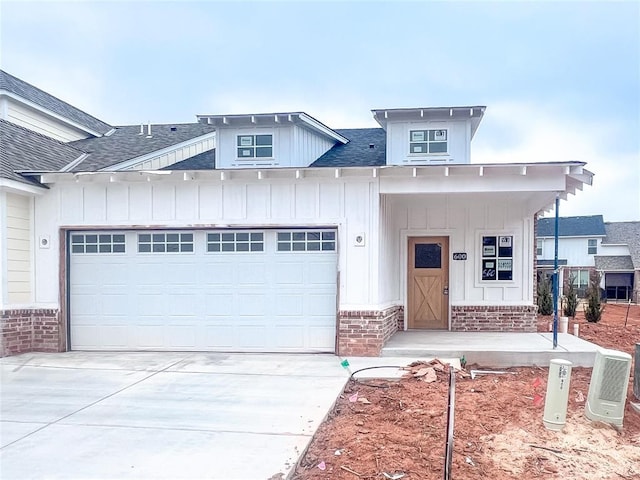 modern farmhouse featuring roof with shingles, an attached garage, concrete driveway, board and batten siding, and brick siding