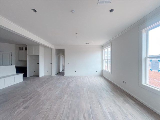 unfurnished living room featuring crown molding, plenty of natural light, baseboards, and light wood-type flooring