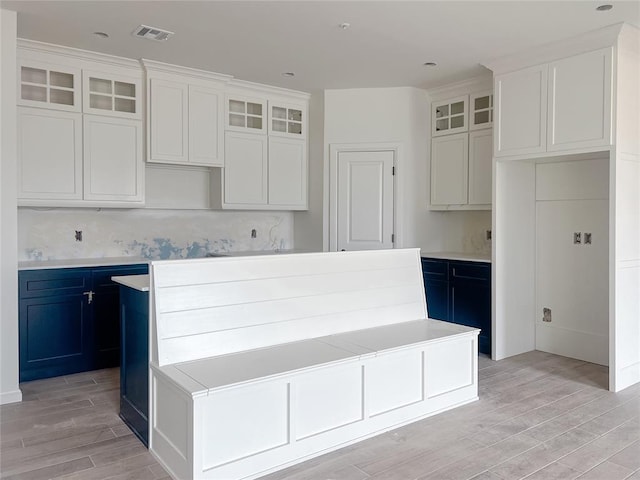 kitchen with visible vents, glass insert cabinets, a kitchen island, and wood tiled floor