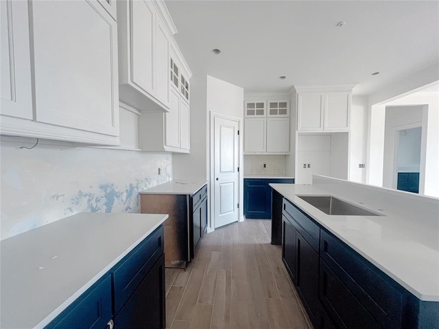 kitchen featuring glass insert cabinets, an island with sink, wood finished floors, white cabinetry, and a sink