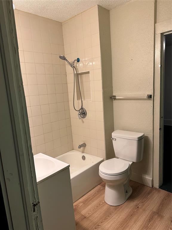 full bathroom with vanity, a textured ceiling, tiled shower / bath combo, hardwood / wood-style floors, and toilet