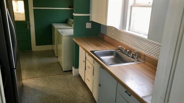 kitchen with washer and dryer, white cabinetry, stainless steel refrigerator, and sink