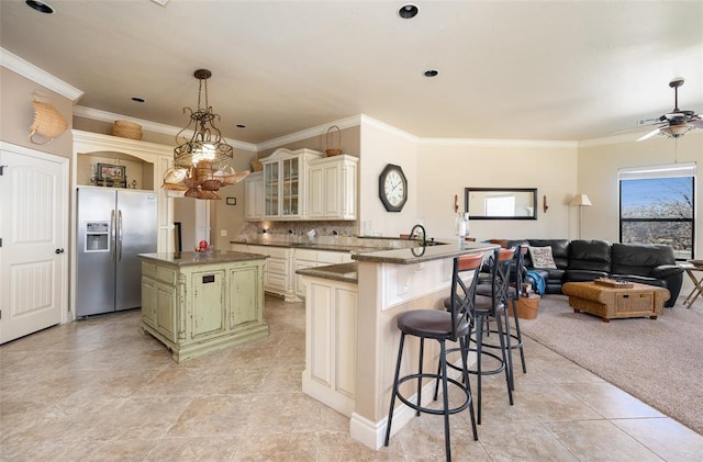 kitchen featuring kitchen peninsula, stainless steel fridge, cream cabinets, a breakfast bar, and a kitchen island