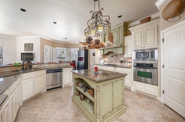 kitchen featuring stainless steel appliances, sink, cream cabinets, decorative light fixtures, and a center island