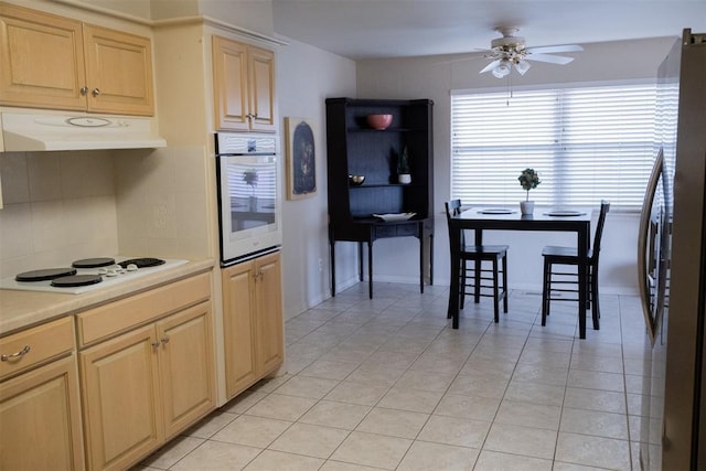 kitchen with light brown cabinetry, white appliances, ceiling fan, and light tile patterned flooring