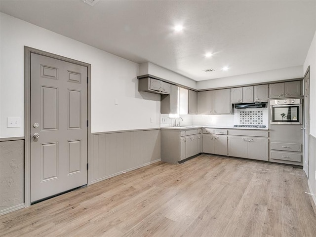 kitchen with gray cabinets, light wood-type flooring, stainless steel oven, and sink