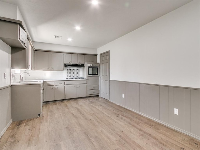 kitchen with gray cabinetry, gas stovetop, sink, light hardwood / wood-style flooring, and oven