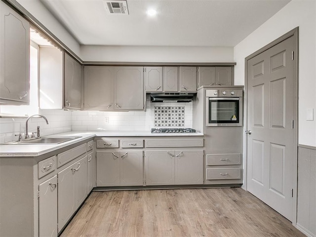 kitchen featuring gray cabinetry, sink, stainless steel appliances, tasteful backsplash, and light hardwood / wood-style floors