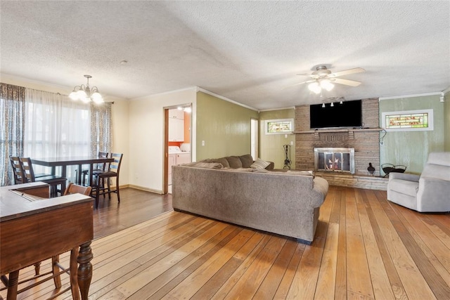 living room featuring a brick fireplace, a textured ceiling, ceiling fan with notable chandelier, crown molding, and hardwood / wood-style flooring