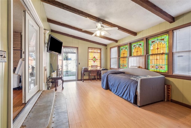 bedroom with access to outside, lofted ceiling with beams, ceiling fan, light wood-type flooring, and a textured ceiling