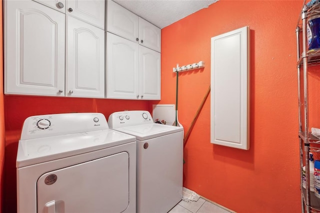 clothes washing area with light tile patterned flooring, cabinets, a textured ceiling, and independent washer and dryer