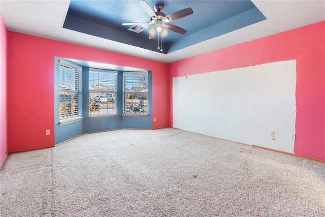 empty room with carpet flooring, a tray ceiling, and ceiling fan