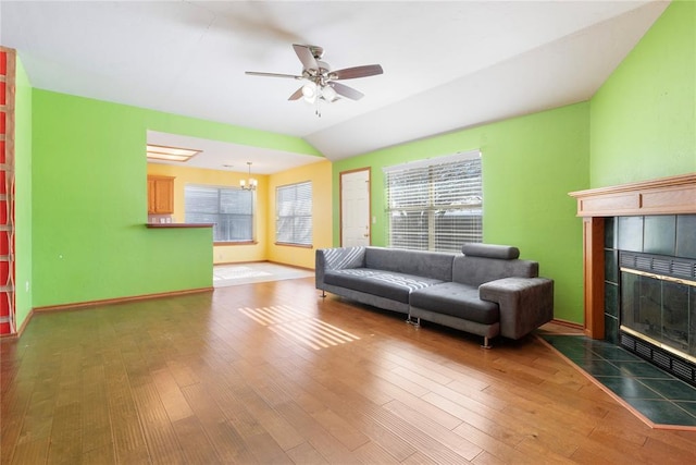 living room featuring dark hardwood / wood-style floors, ceiling fan with notable chandelier, a tile fireplace, and vaulted ceiling