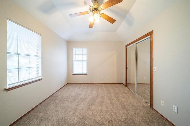 unfurnished bedroom featuring light colored carpet, a raised ceiling, ceiling fan, vaulted ceiling, and a closet