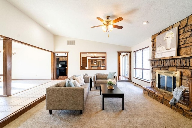 living room with ceiling fan, a stone fireplace, a textured ceiling, vaulted ceiling, and carpet