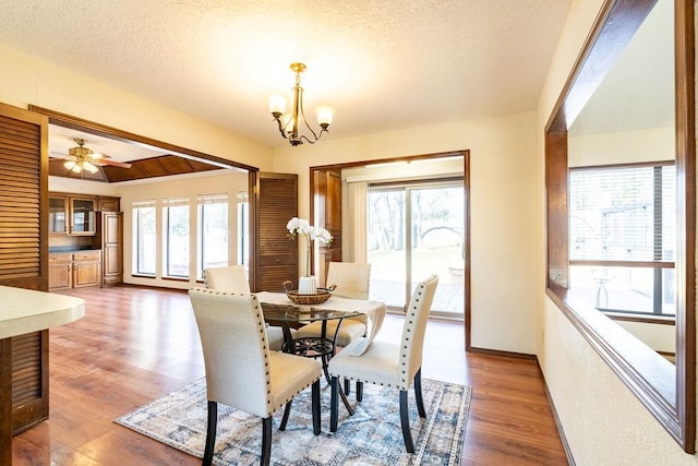 dining space with ceiling fan with notable chandelier, wood-type flooring, a textured ceiling, and a wealth of natural light