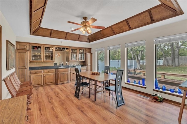 dining room with a raised ceiling, bar, ceiling fan, and light hardwood / wood-style flooring
