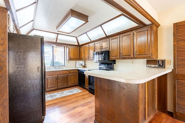 kitchen featuring kitchen peninsula, sink, black appliances, and light wood-type flooring