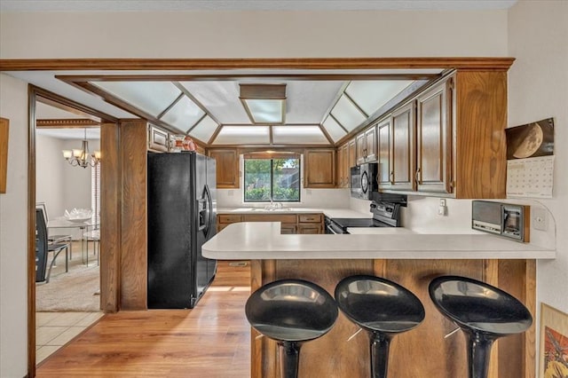 kitchen with sink, a kitchen breakfast bar, kitchen peninsula, a chandelier, and black appliances