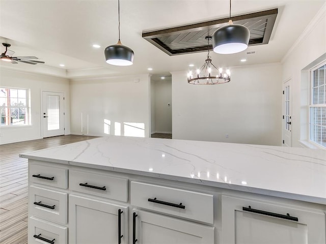 kitchen featuring light stone counters, white cabinets, decorative light fixtures, and ceiling fan with notable chandelier