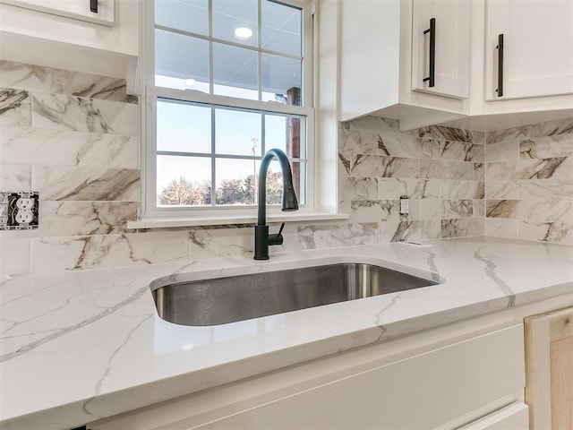 details with white cabinetry, backsplash, light stone counters, and sink