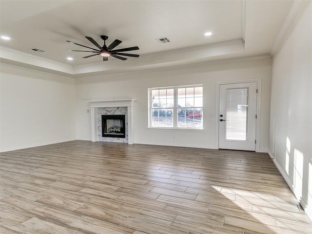 unfurnished living room featuring a high end fireplace, a raised ceiling, ceiling fan, and ornamental molding