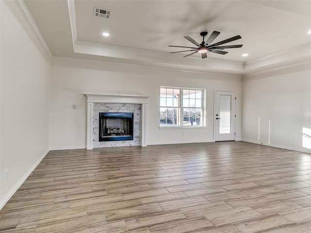 unfurnished living room featuring ceiling fan, a raised ceiling, a fireplace, and crown molding