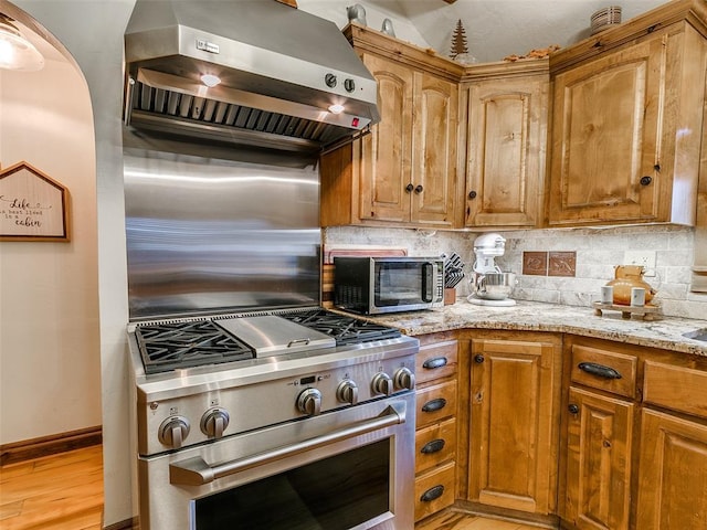 kitchen featuring wall chimney exhaust hood, stainless steel range, tasteful backsplash, light hardwood / wood-style floors, and light stone counters