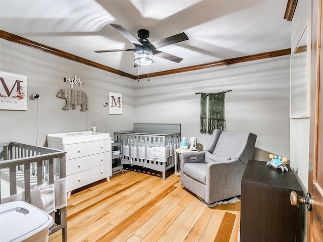 bedroom with a crib, light hardwood / wood-style floors, ceiling fan, and ornamental molding