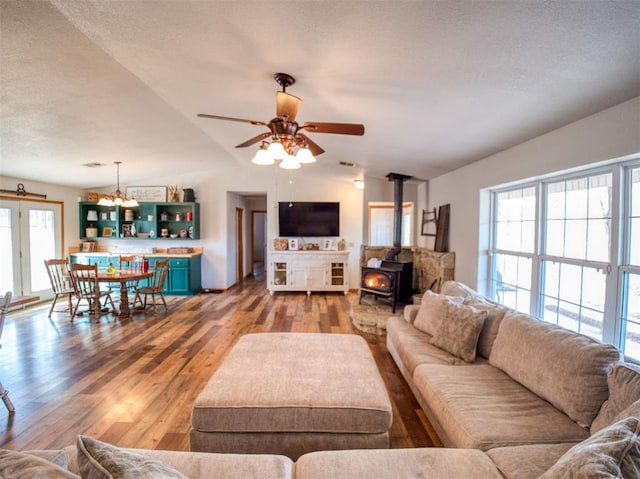 living room featuring a wood stove, wood-type flooring, a textured ceiling, vaulted ceiling, and ceiling fan with notable chandelier