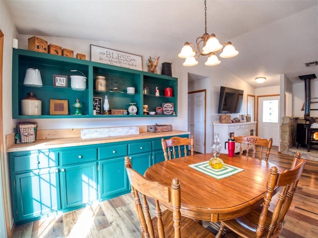 dining space featuring a wood stove, a notable chandelier, vaulted ceiling, and light wood-type flooring