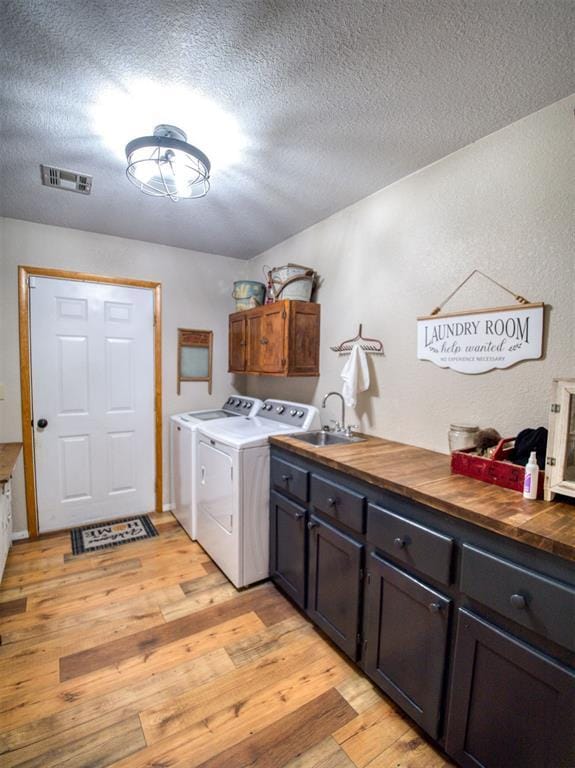 laundry room featuring washer and clothes dryer, cabinets, sink, a textured ceiling, and light hardwood / wood-style floors