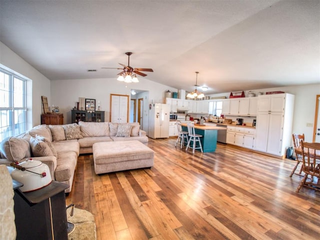 living room with ceiling fan with notable chandelier, light wood-type flooring, and lofted ceiling