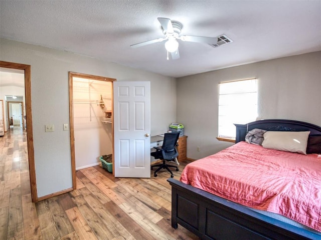 bedroom featuring a spacious closet, ceiling fan, a textured ceiling, a closet, and light wood-type flooring