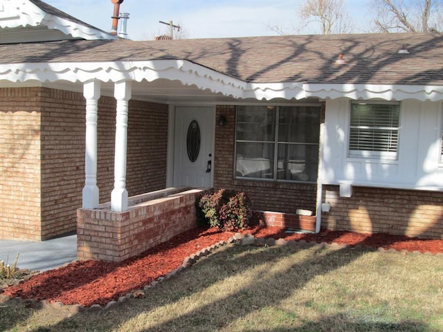 property entrance featuring covered porch, brick siding, and roof with shingles