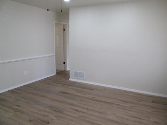 empty room featuring baseboards, visible vents, and wood finished floors