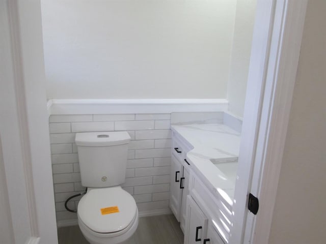 half bathroom with tile walls, wainscoting, vanity, and toilet