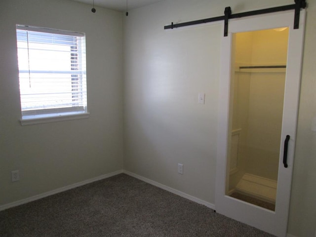 unfurnished bedroom with carpet floors, a barn door, and baseboards