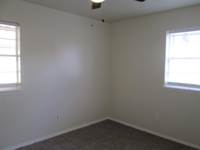 spare room with ceiling fan, dark colored carpet, and baseboards