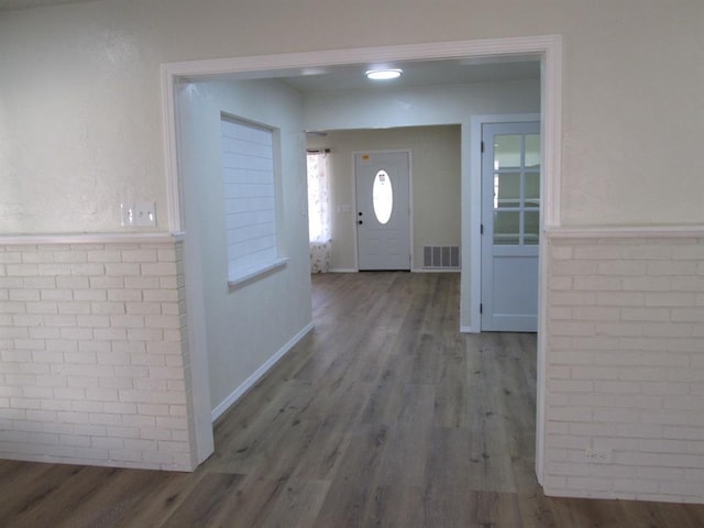 foyer entrance featuring baseboards, visible vents, brick wall, and wood finished floors