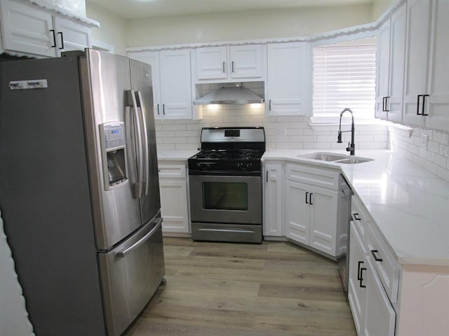 kitchen with stainless steel appliances, a sink, exhaust hood, white cabinets, and light wood-type flooring