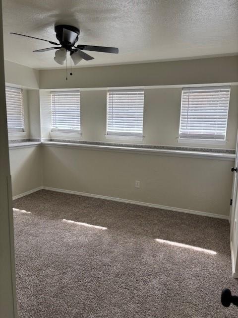 carpeted spare room featuring a textured ceiling, a ceiling fan, and baseboards