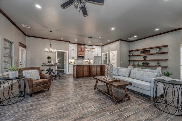 living room featuring ceiling fan with notable chandelier, crown molding, and sink