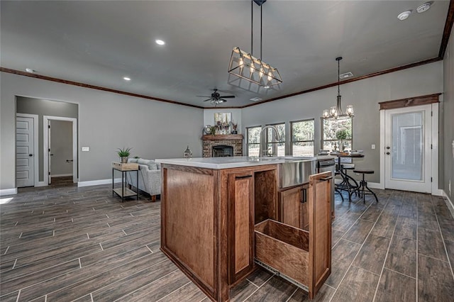 kitchen with ceiling fan with notable chandelier, crown molding, decorative light fixtures, a center island with sink, and a fireplace