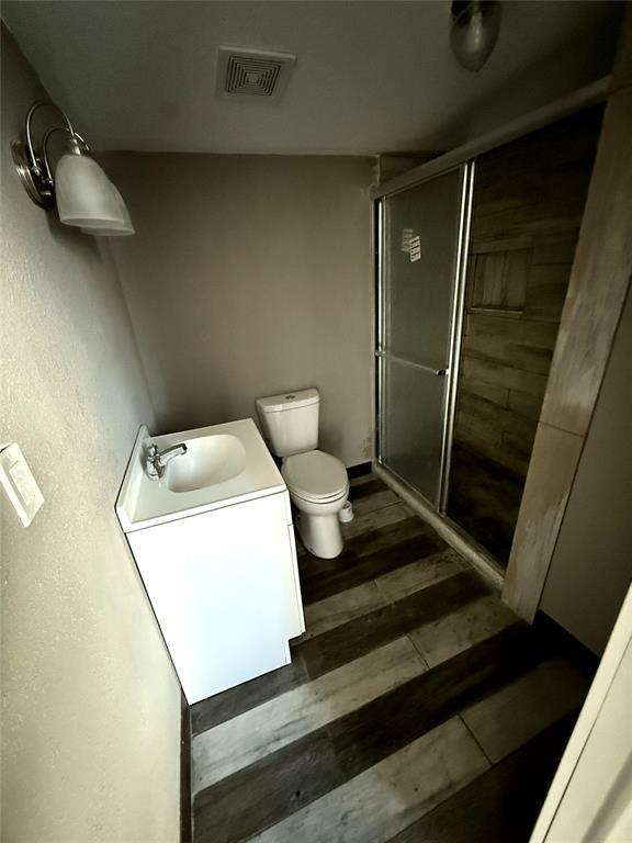 bathroom with toilet, wood-type flooring, a shower with shower door, and vanity